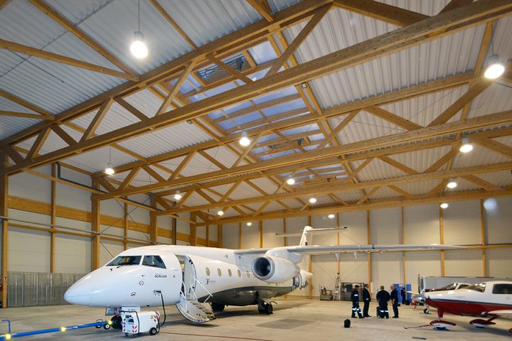 Innenansicht eines Flugzeughangars mit einem geparkten Regionaljet und sichtbarer Holzfachwerk-Dachkonstruktion.
