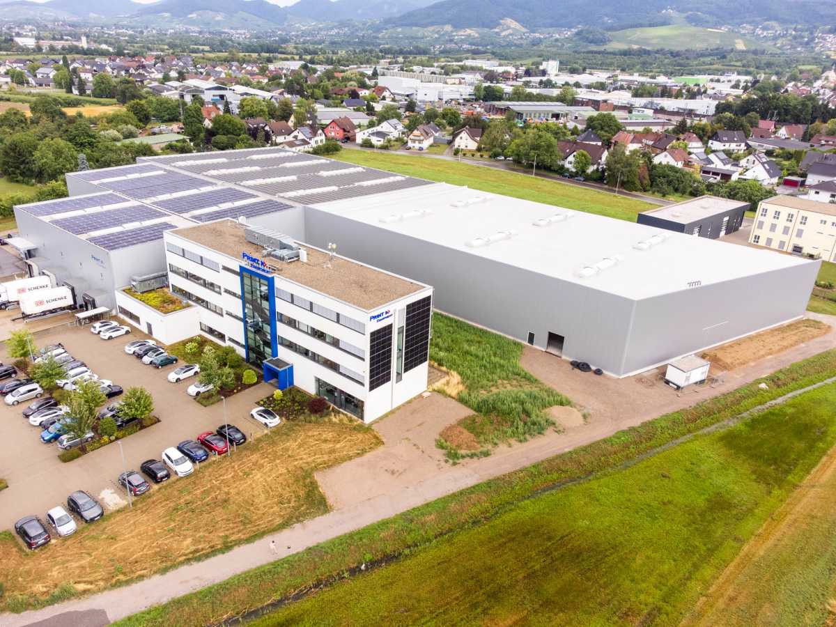 Luftaufnahme der Logistikhalle in Ottersweier mit vorgelagertem Bürogebäude, Photovoltaikanlage auf dem Hallendach und umgebender Ortschaft.