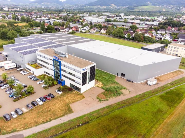 Luftaufnahme der Logistikhalle in Ottersweier mit vorgelagertem Bürogebäude, Photovoltaikanlage auf dem Hallendach und umgebender Ortschaft.