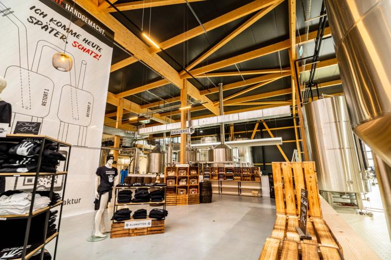 Manufaktur-Innenraum mit Wandgrafik und sichtbaren Fachwerkbindern aus Holz, rechts die Edelstahl-Brauanlage