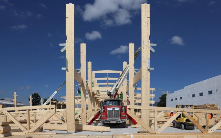 Holztragwerk im Bau, ein roter Autokran hebt ein Bauteil ein