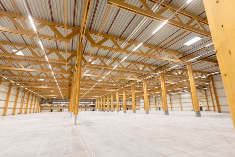 Weitwinklige Innenaufnahme entlang der Längsachse der Halle mit Holzstützen und Fachwerkträgern in der Flucht sowie durchgehender LED-Beleuchtung.