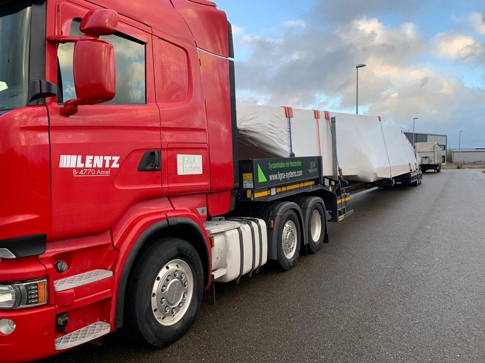 Roter LENTZ-Sattelzug mit Auflieger von LIGNA systems transportiert verpackte Holzbauteile einer Systemhalle