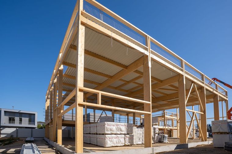 Angle du bâtiment en gros œuvre à Courtry : poteaux et poutres en lamellé-collé avec écharpes diagonales, filets de protection tendus entre les poutres, la toiture déjà couverte en bac acier