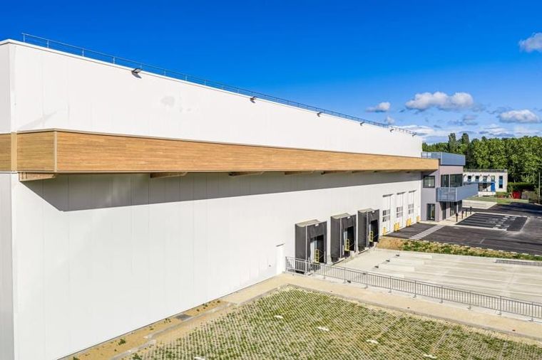 Längsseite der Halle mit weißer Fassade, hölzernem Fassadenband und Verladehof
