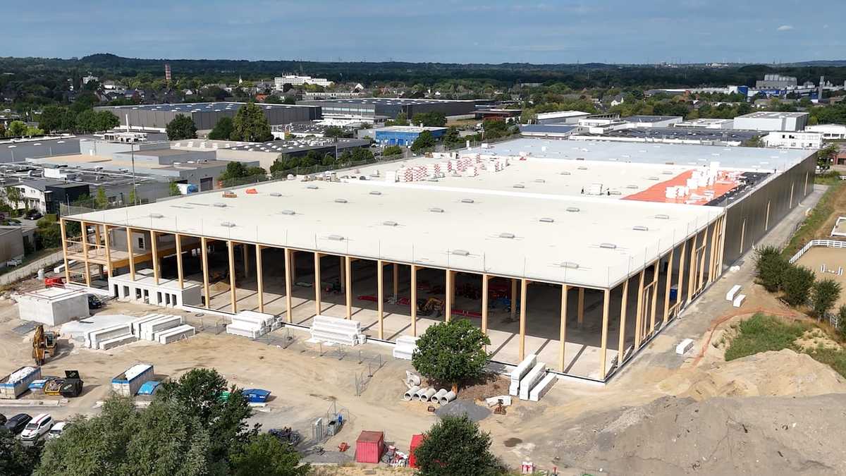 Luftaufnahme der Logistikhalle in Mönchengladbach im Bau, das Tragwerk aus Holz steht und die Dachfläche ist größtenteils eingedeckt, dahinter das Gewerbegebiet