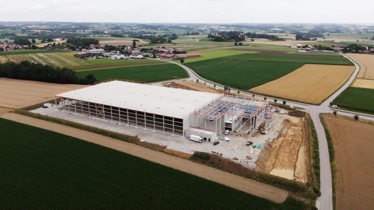 Aerial view of the hall under construction, the roof is largely closed, the timber trusses are still exposed at the gable end