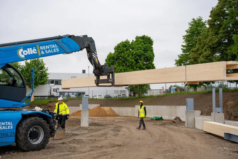 Monteure handhaben ein Holzbauteil mit dem Teleskoplader auf der Baustelle