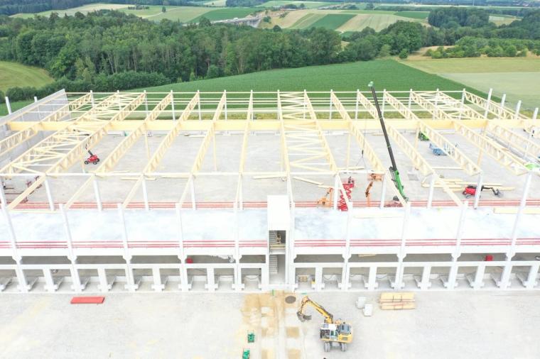 Top-down aerial view of the timber trusses being erected above the concrete frame, with a mobile crane and lifts on the floor slab