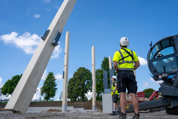Monteur an einer aufgerichteten Holz-Rohrstütze, Bagger im Hintergrund