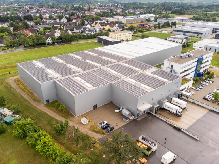 Luftaufnahme der Hallenrückseite in Ottersweier mit großflächiger Photovoltaikanlage auf dem Dach, angedockten Lkw an den Ladetoren und seitlichem Bürogebäude.
