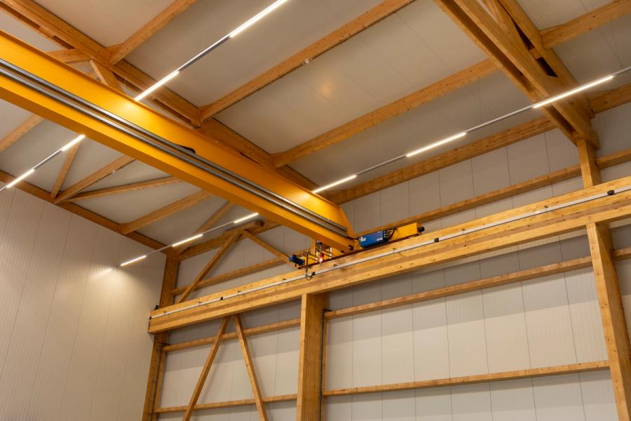 Gelber Brückenkran auf der Kranbahn, getragen vom Holztragwerk einer Gewerbehalle, mit Holzstützen und Dachbindern