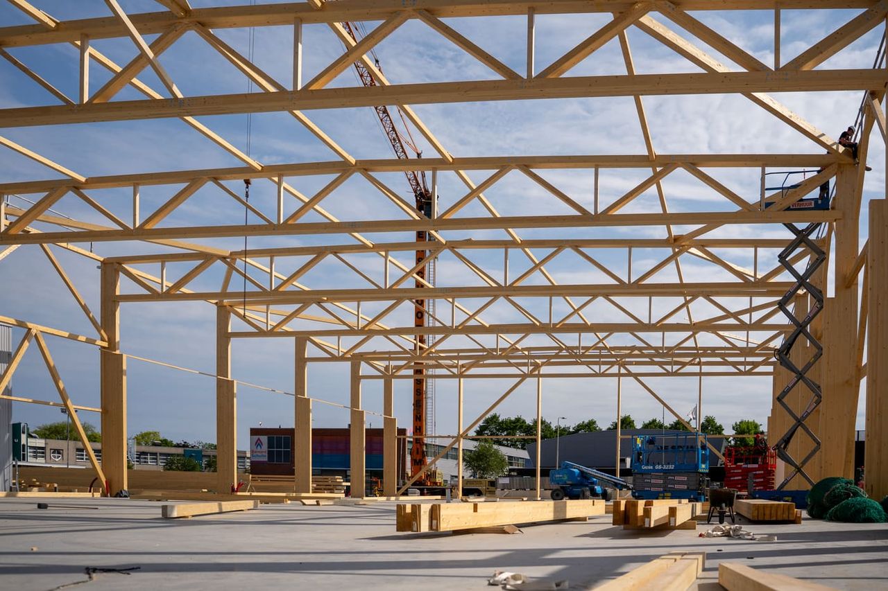 Wide-span timber truss structure of a hall under construction against a blue sky, erection with crane