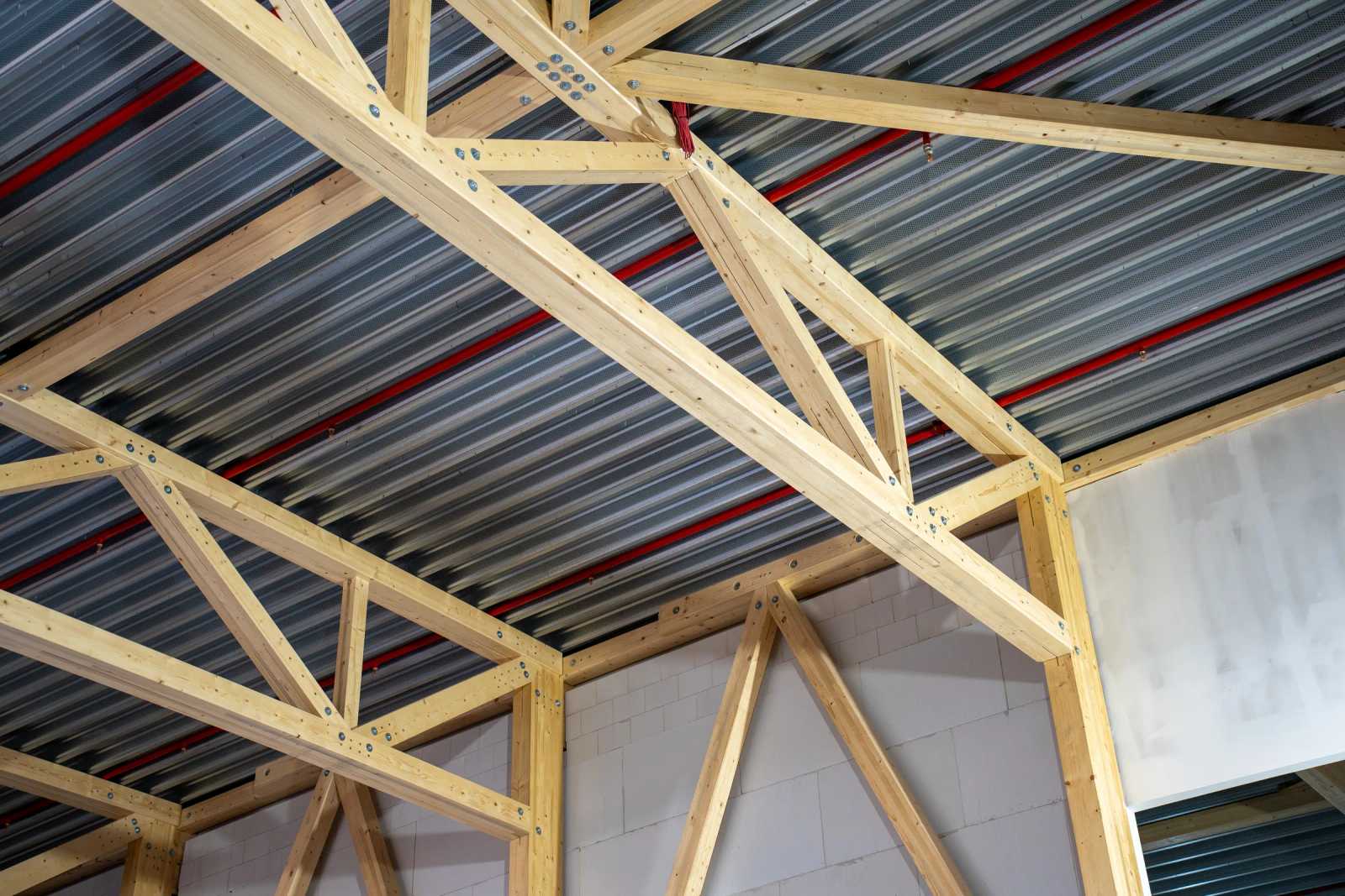 Untersicht der Holz-Fachwerkbinder im Halleninnenraum mit Trapezblech-Dach