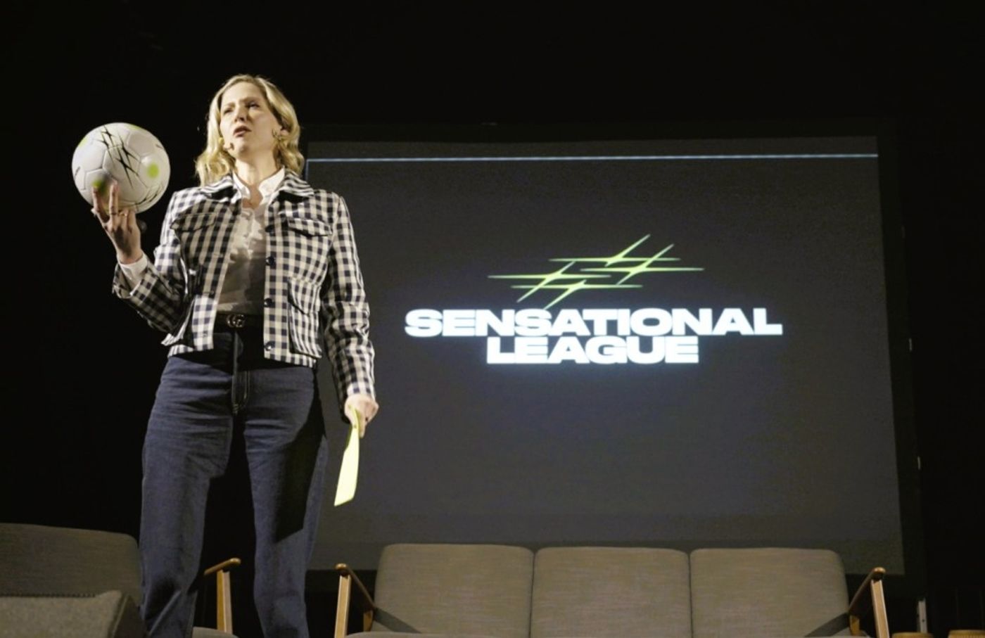 Bettina Kuperman on stage at Spot On Activation 2026, holding a Sensational Ball, with the Sensational League logo behind her.