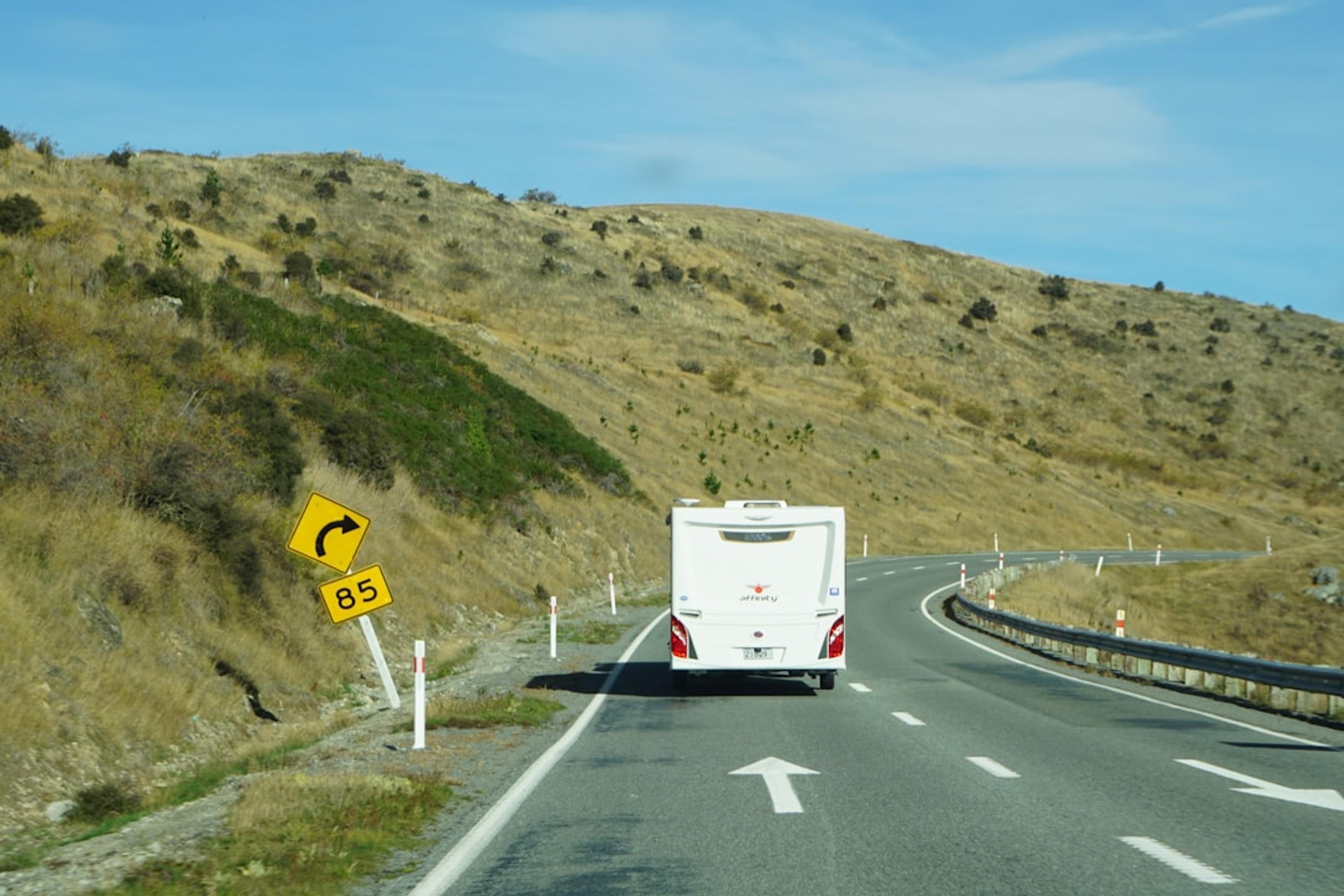 A white campervan drives on a winding road.