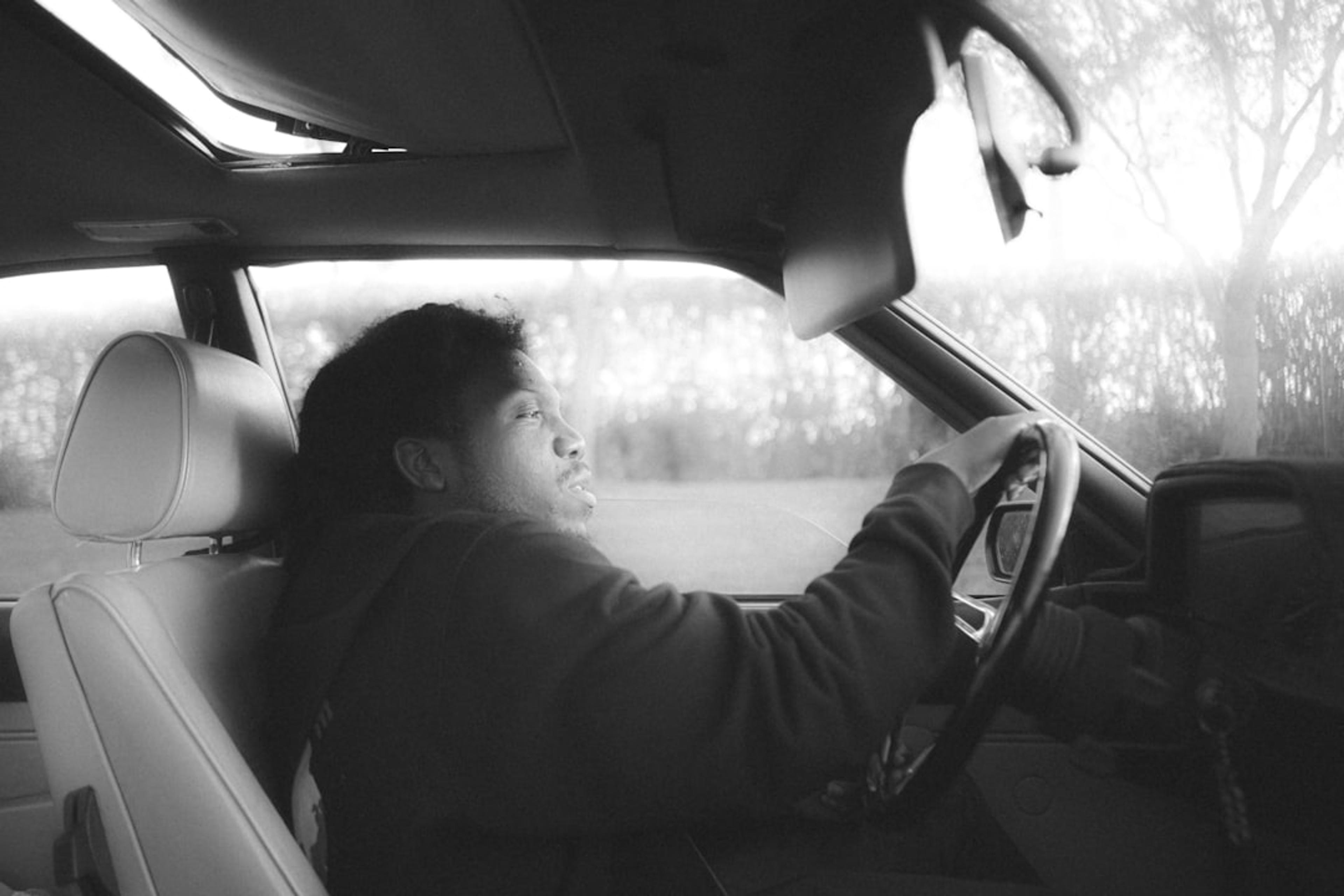 a man sitting in a car with his hand on the steering wheel