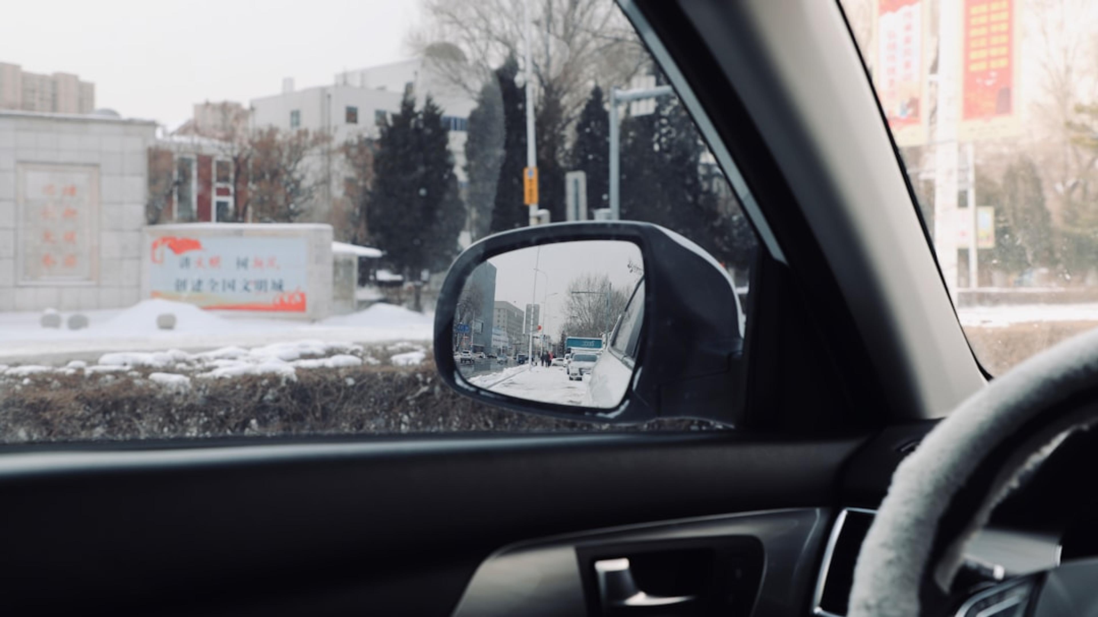 car side mirror showing white car on road during daytime