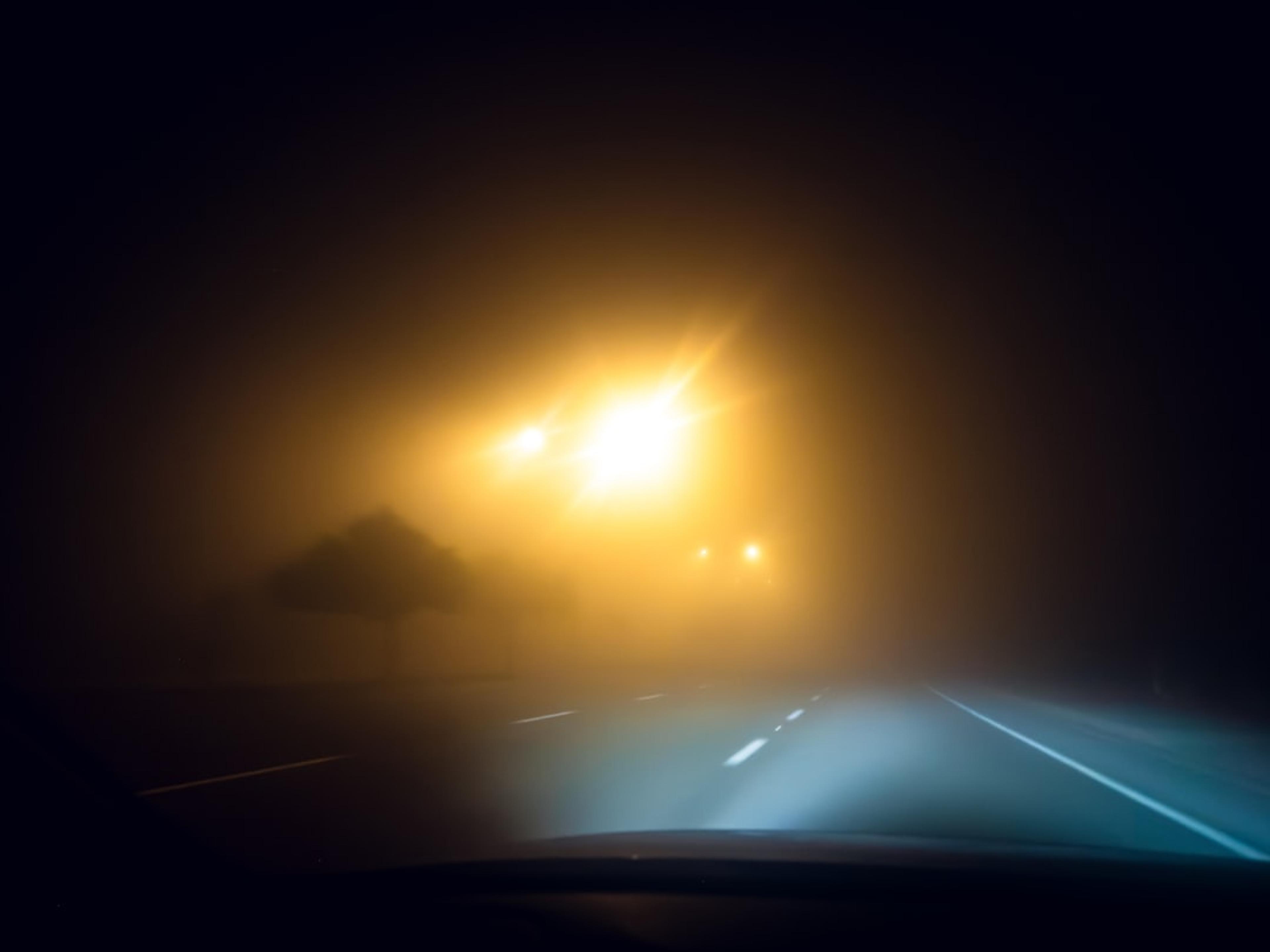 Driving on a foggy road at night with headlights on.