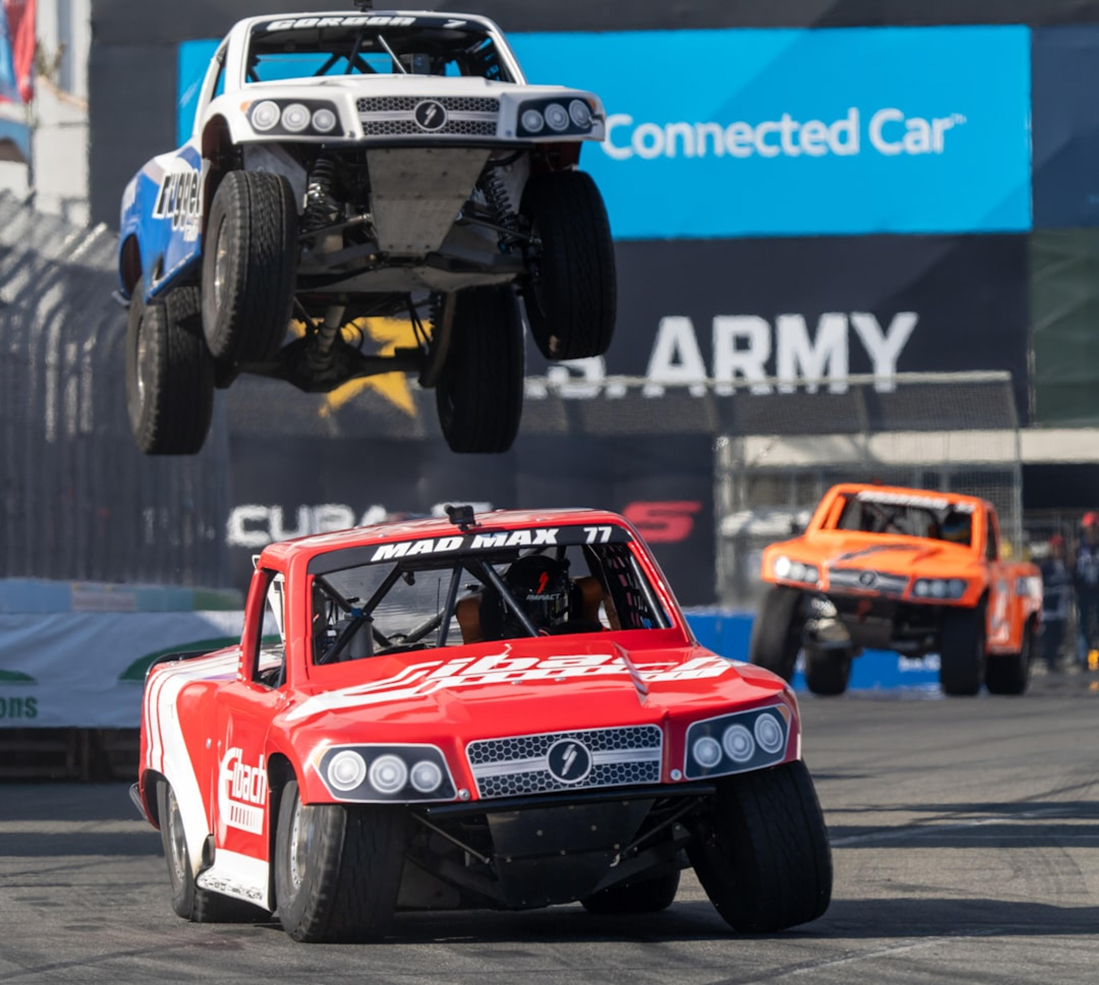 Off-road trucks race, one airborne.