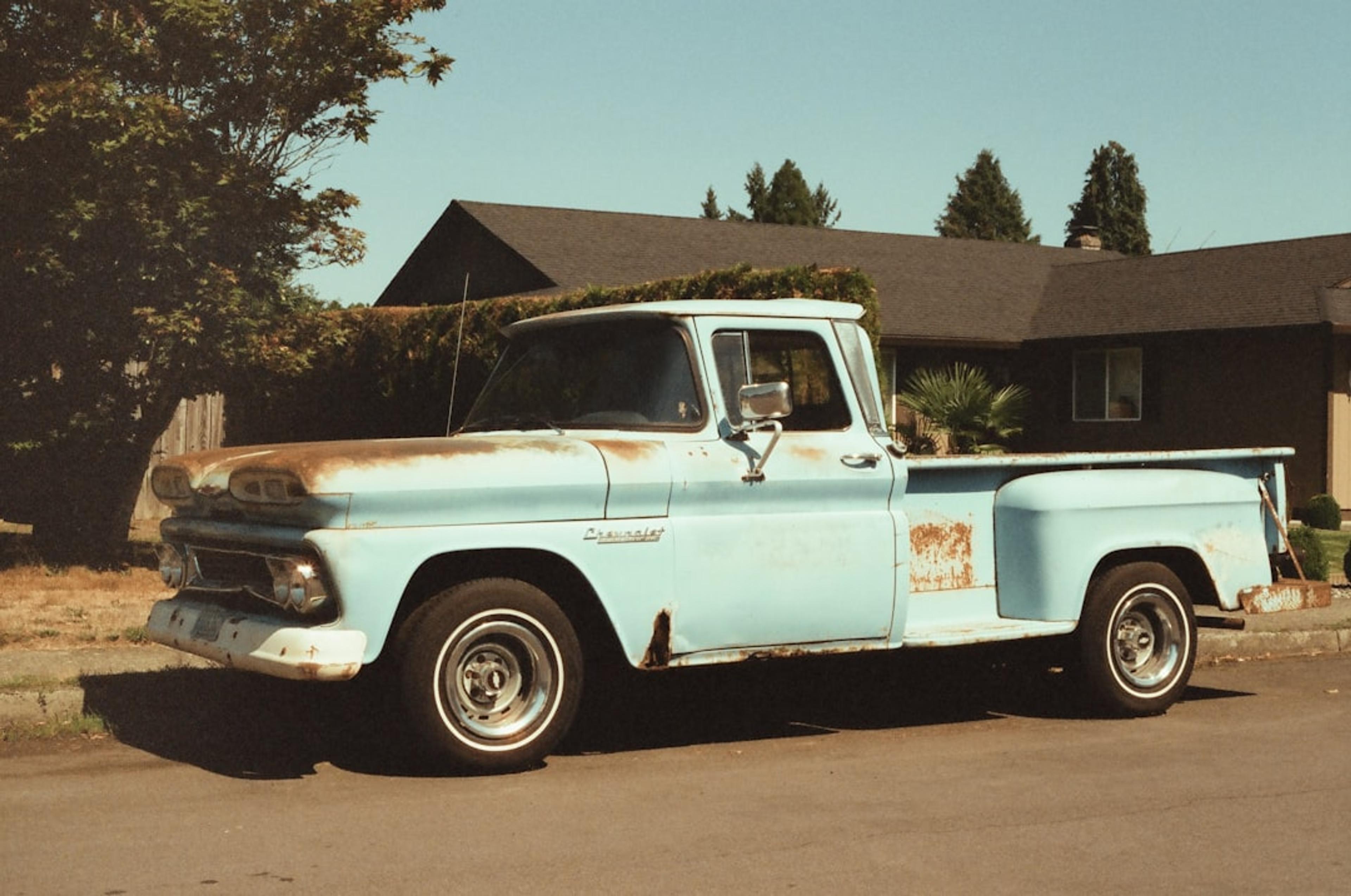 an old blue truck parked in front of a house