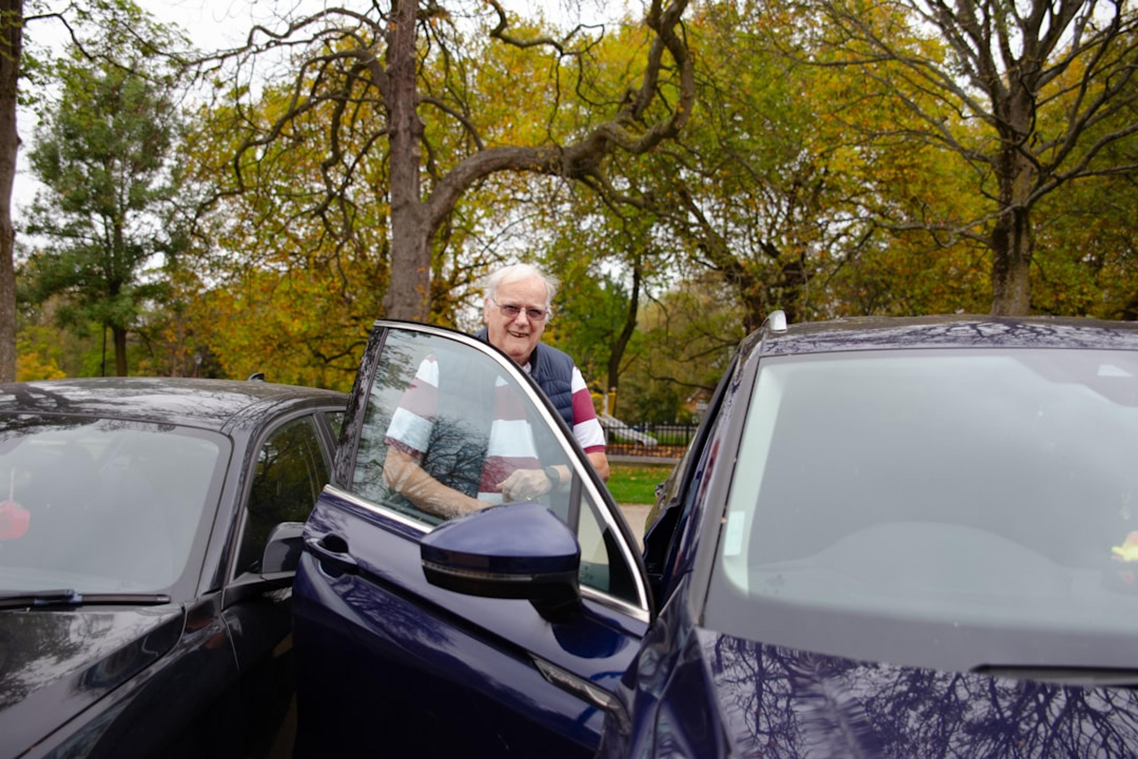 Elderly man standing by an open car door.
