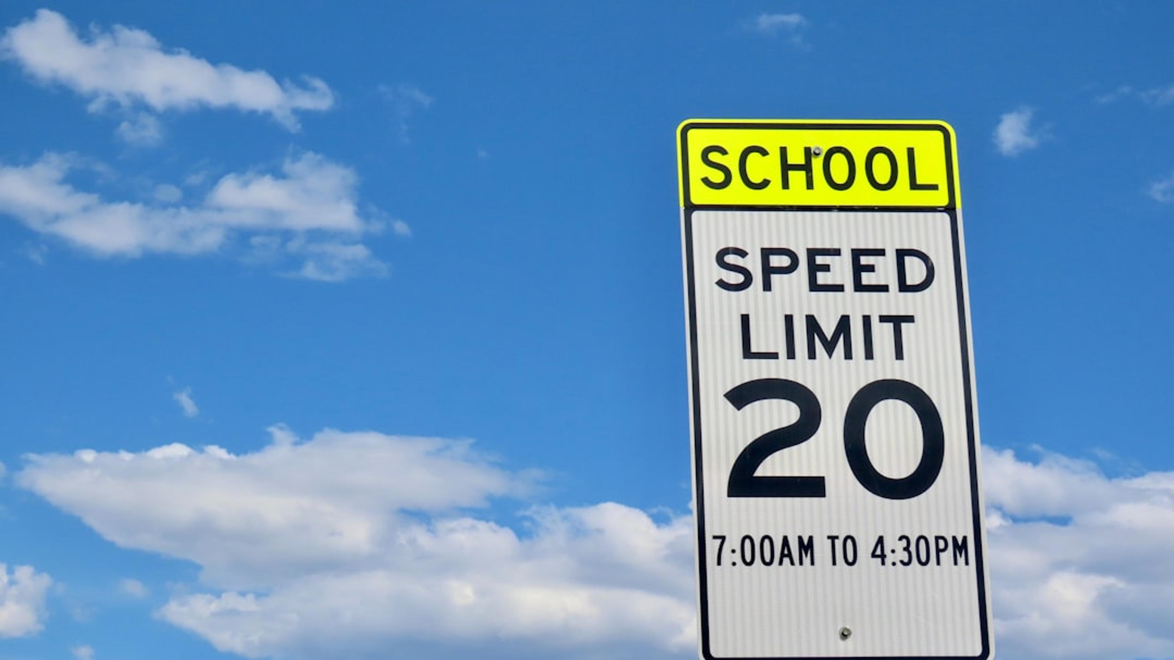 School zone speed limit sign against a cloudy sky.