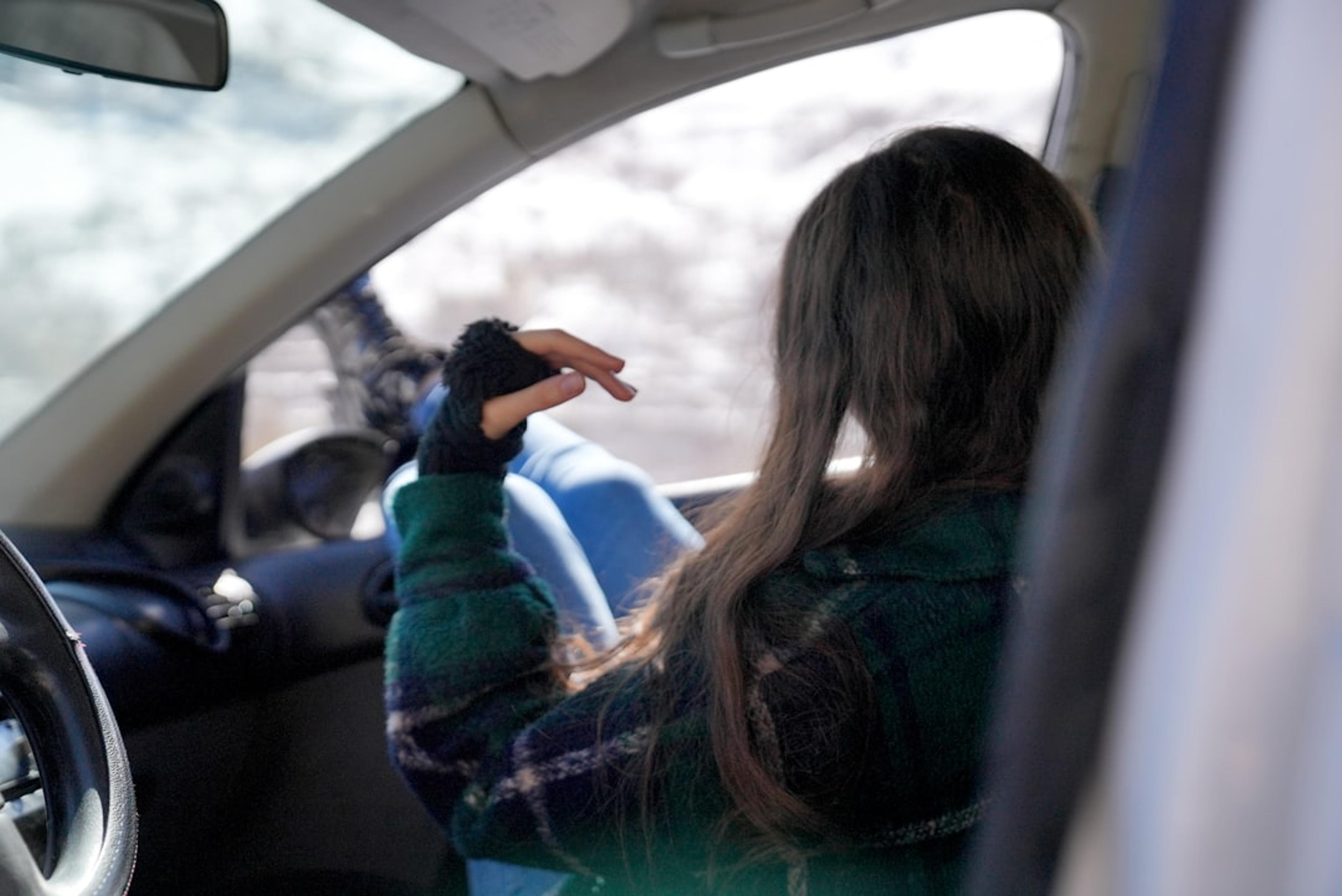 a woman sitting in a car with her hand on the steering wheel
