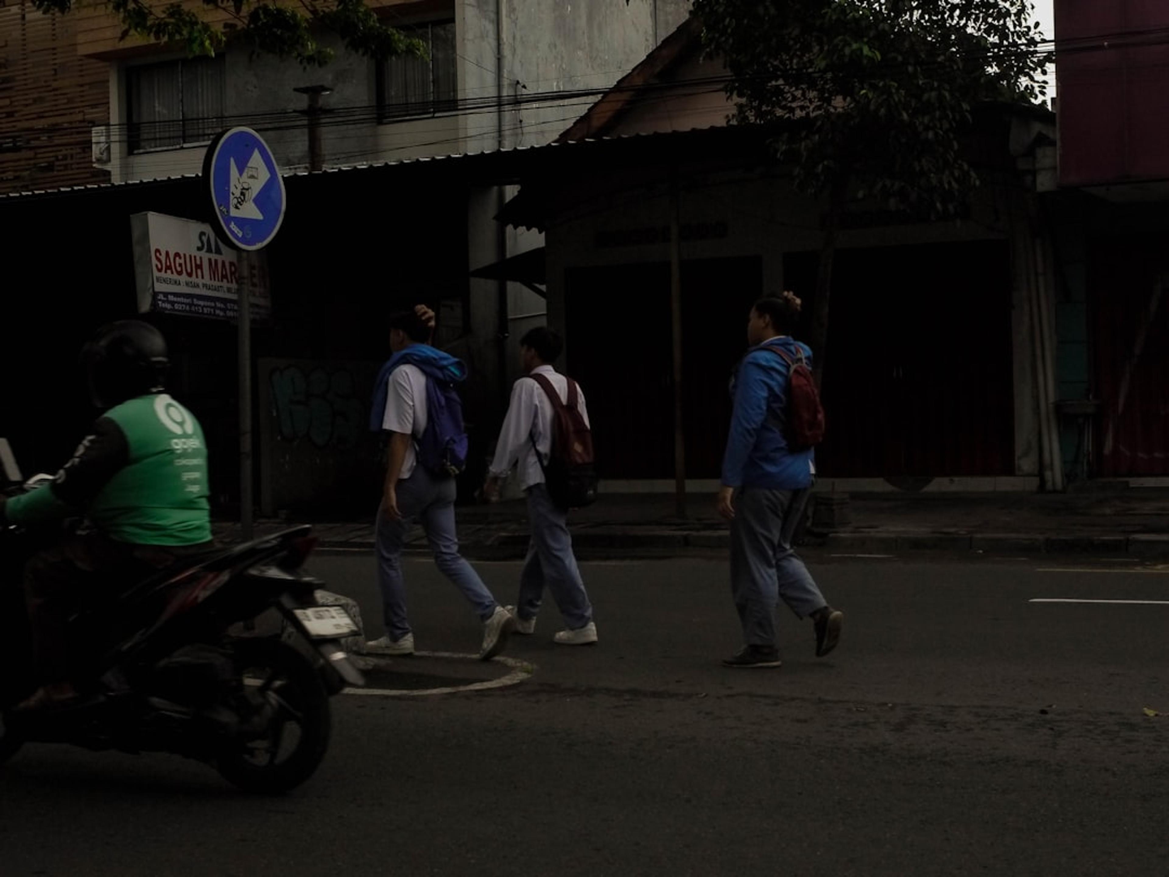 People crossing a street with a motorcycle nearby