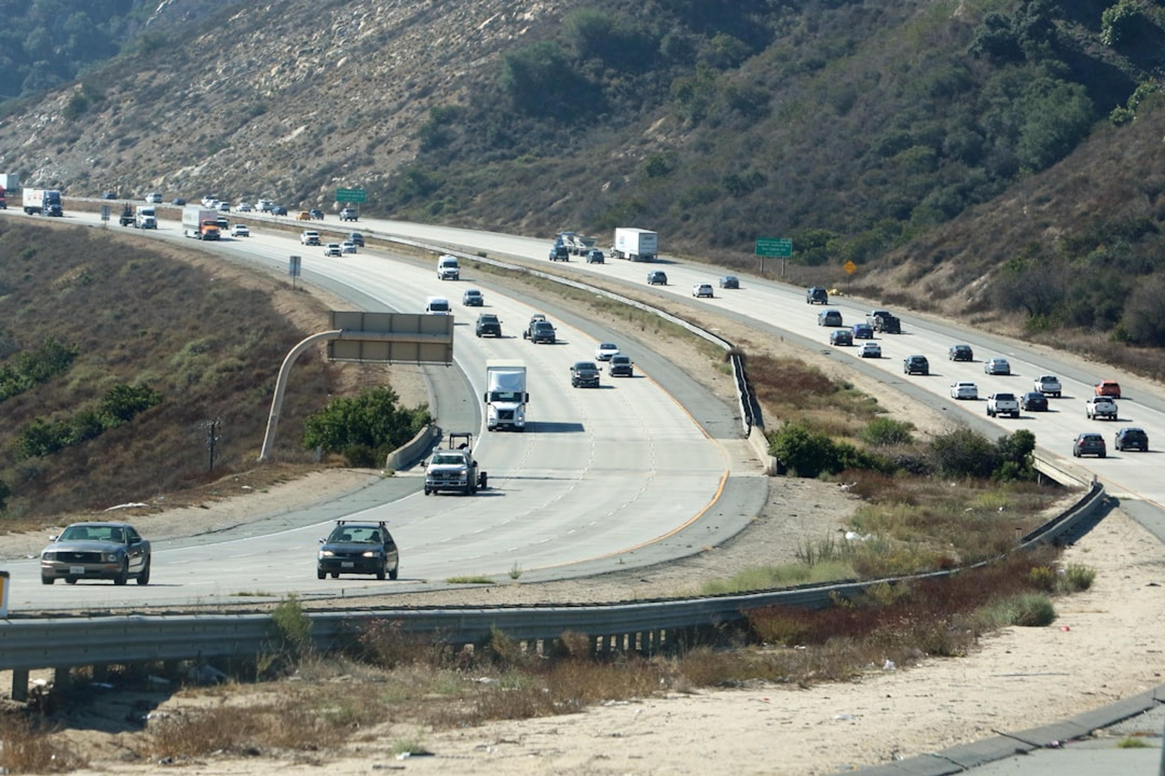 Cars driving on a multi-lane highway through hills.