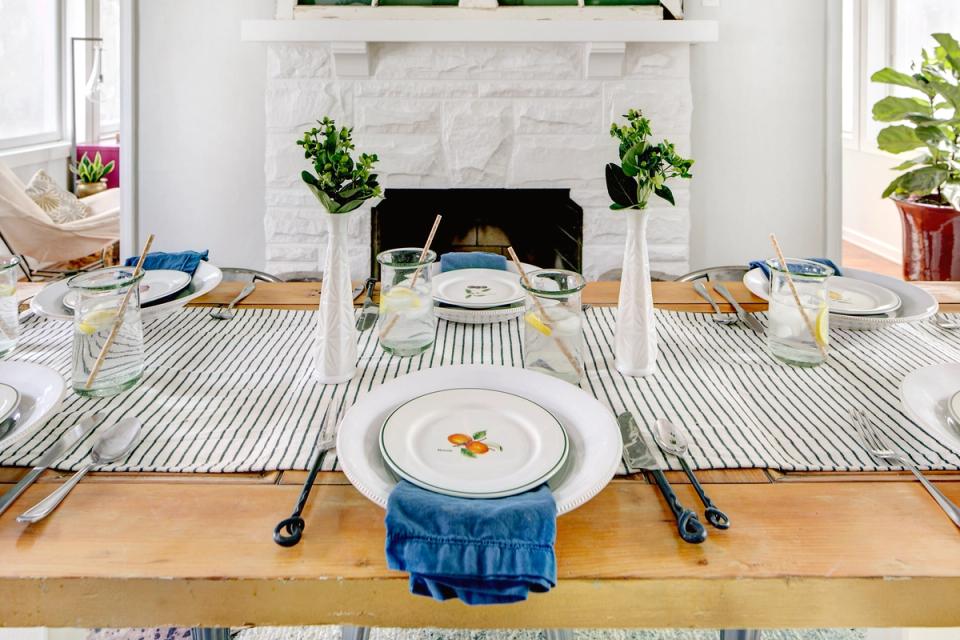 Coastal dining setup with striped runner, white fireplace, and fresh greenery creating an elegant, serene entertaining space.