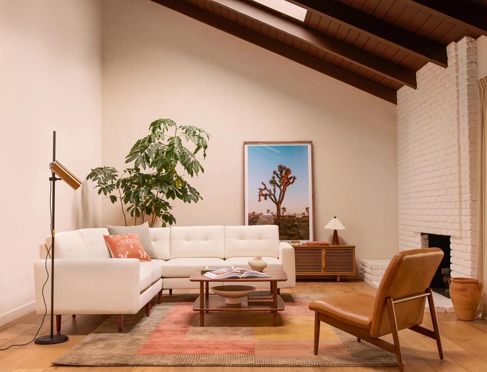 Warm mid-century boho living room with cream sectional, cognac leather chair, exposed beams, and earthy tones.