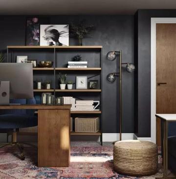 Contemporary office featuring charcoal accent wall, wooden desk, open shelving with brass accents, and jewel-toned chair for refined productivity space