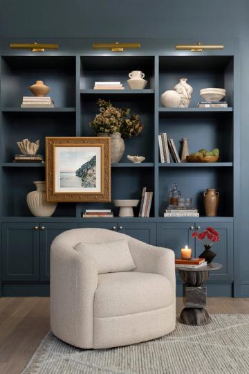 Sophisticated teal shelving wall with brass fixtures, cream armchair, and curated ceramic and book collection