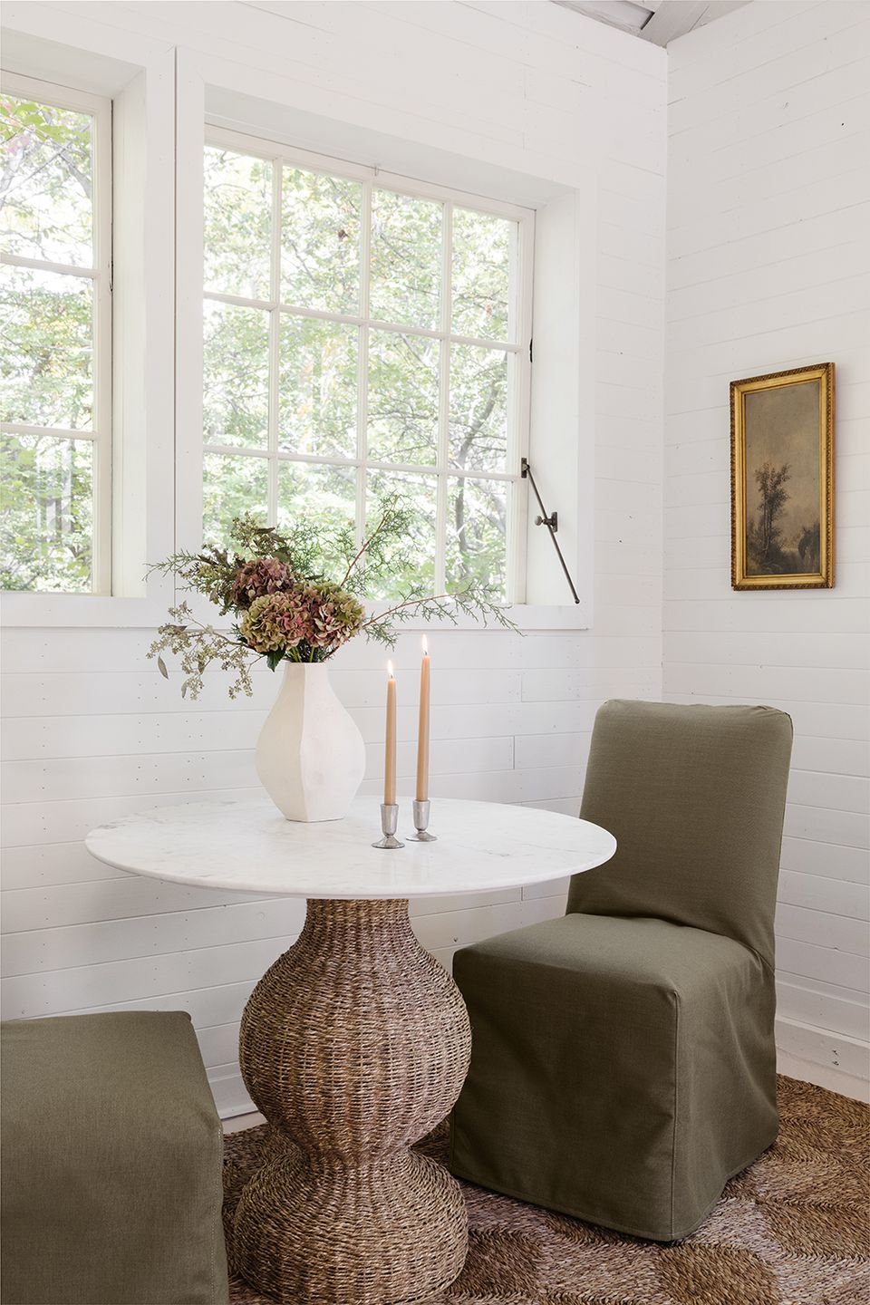Warm minimalist dining area with white round table, woven base, and sage green slip-covered chair
