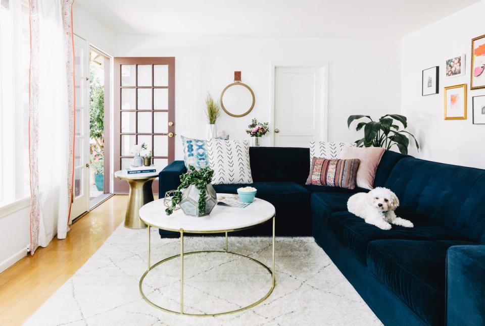 Bright living room with navy velvet sofa, round brass table, geometric rug, and eclectic gallery wall