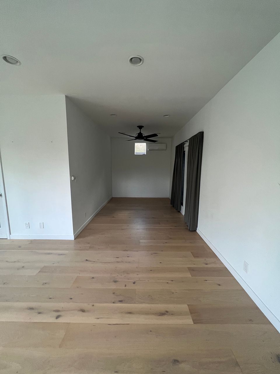 Bright, minimalist empty room with warm wood floors, white walls, and clean lines suggesting calm, contemporary design potential.