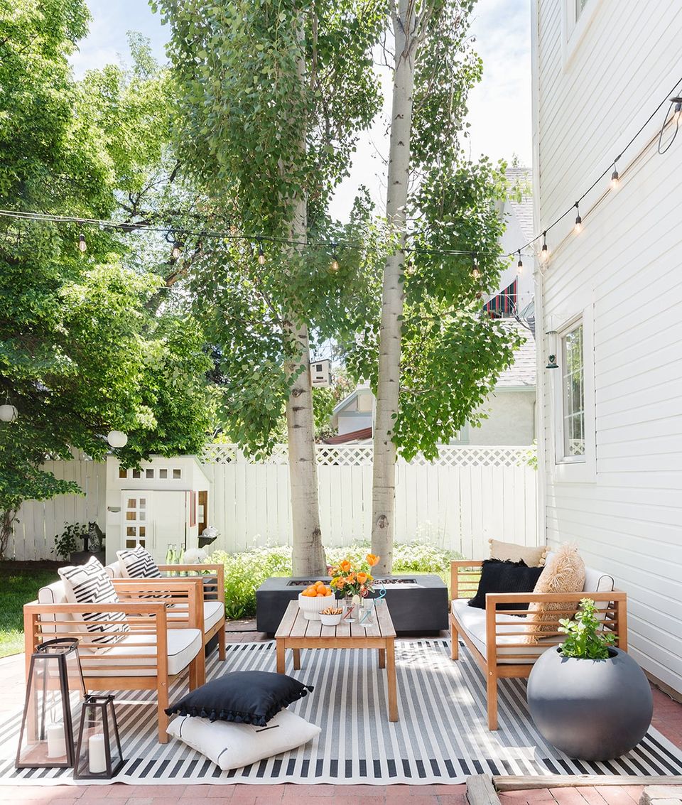 Contemporary patio with striped rug, natural wood furniture, and lush greenery overhead creating a calm, airy retreat.