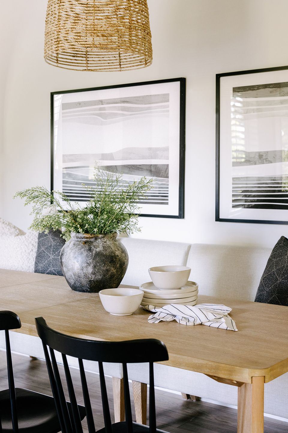 Scandinavian-inspired dining table with natural wood, woven pendant light, black chairs, and abstract wall art