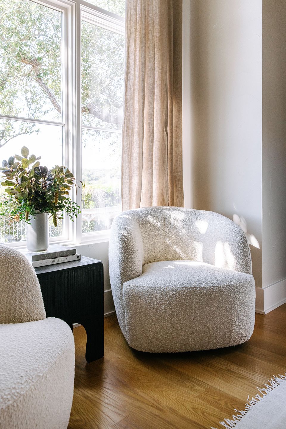 Minimalist sunlit reading area with cream boucle chairs, warm wood floors, and soft natural light from large windows.