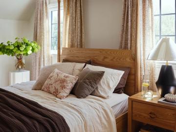 Warm traditional bedroom with natural wood bed frame, layered textiles, and neutral linen drapery