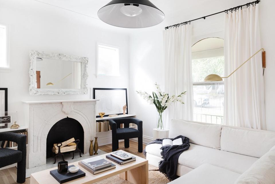 Minimalist bedroom with Scandinavian warmth: white walls, black fireplace accent, natural wood, and soft cream bedding