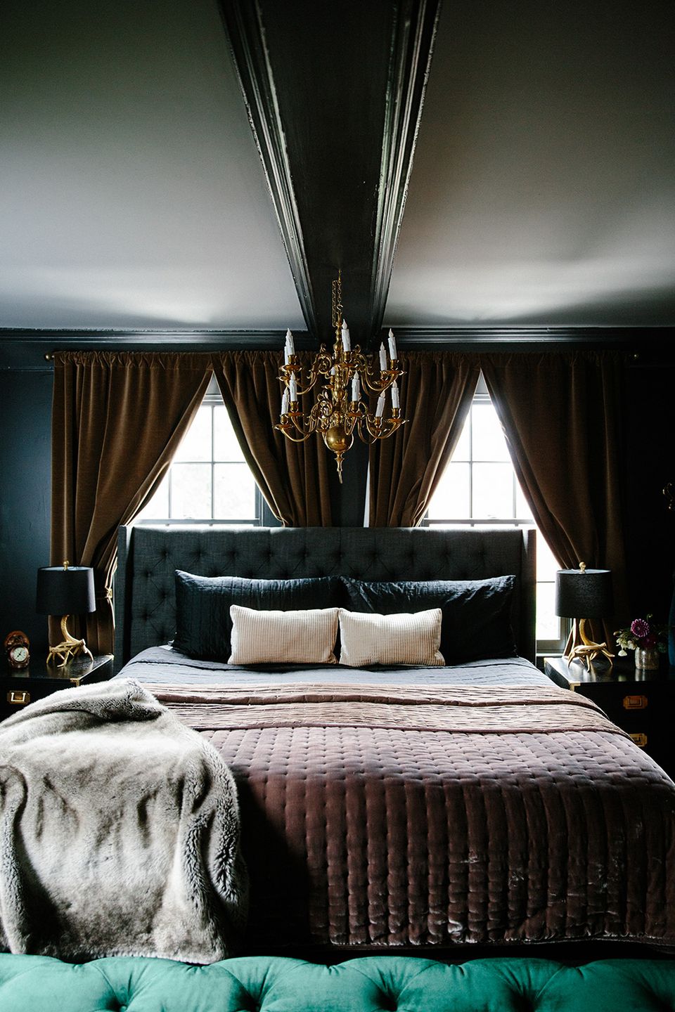 Dramatic dark green bedroom with gold chandelier, emerald headboard, and moody luxe atmosphere
