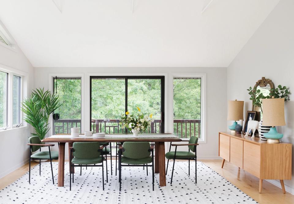 Scandinavian dining room with natural wood table, sage green chairs, soft geometric rug, and abundant greenery creating a warm, nature-inspired aesthetic.