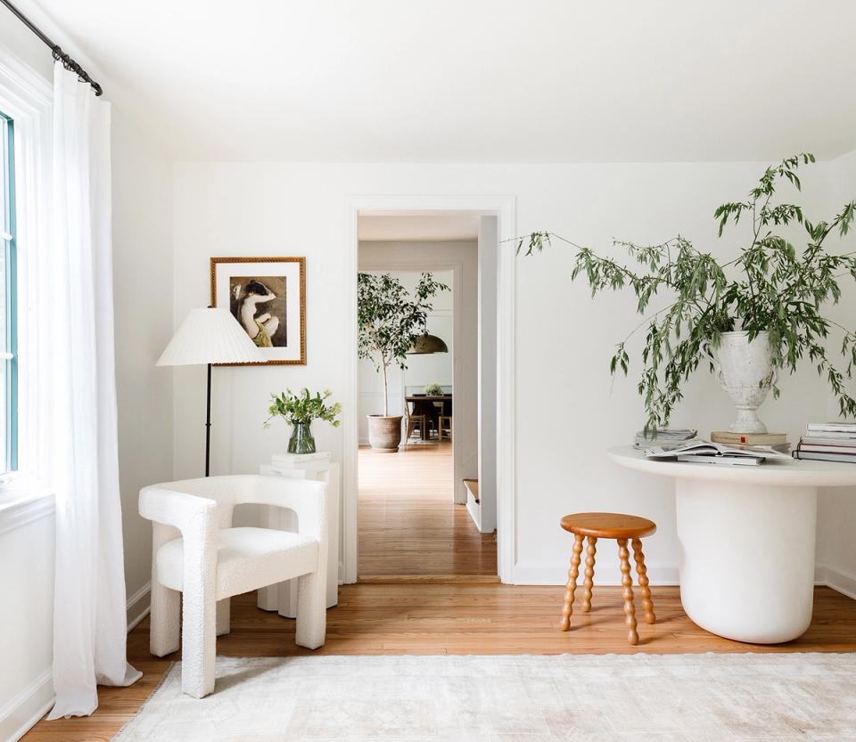 Minimalist entryway with cream curved chair, white cylindrical side table, natural wood accents, and potted greenery
