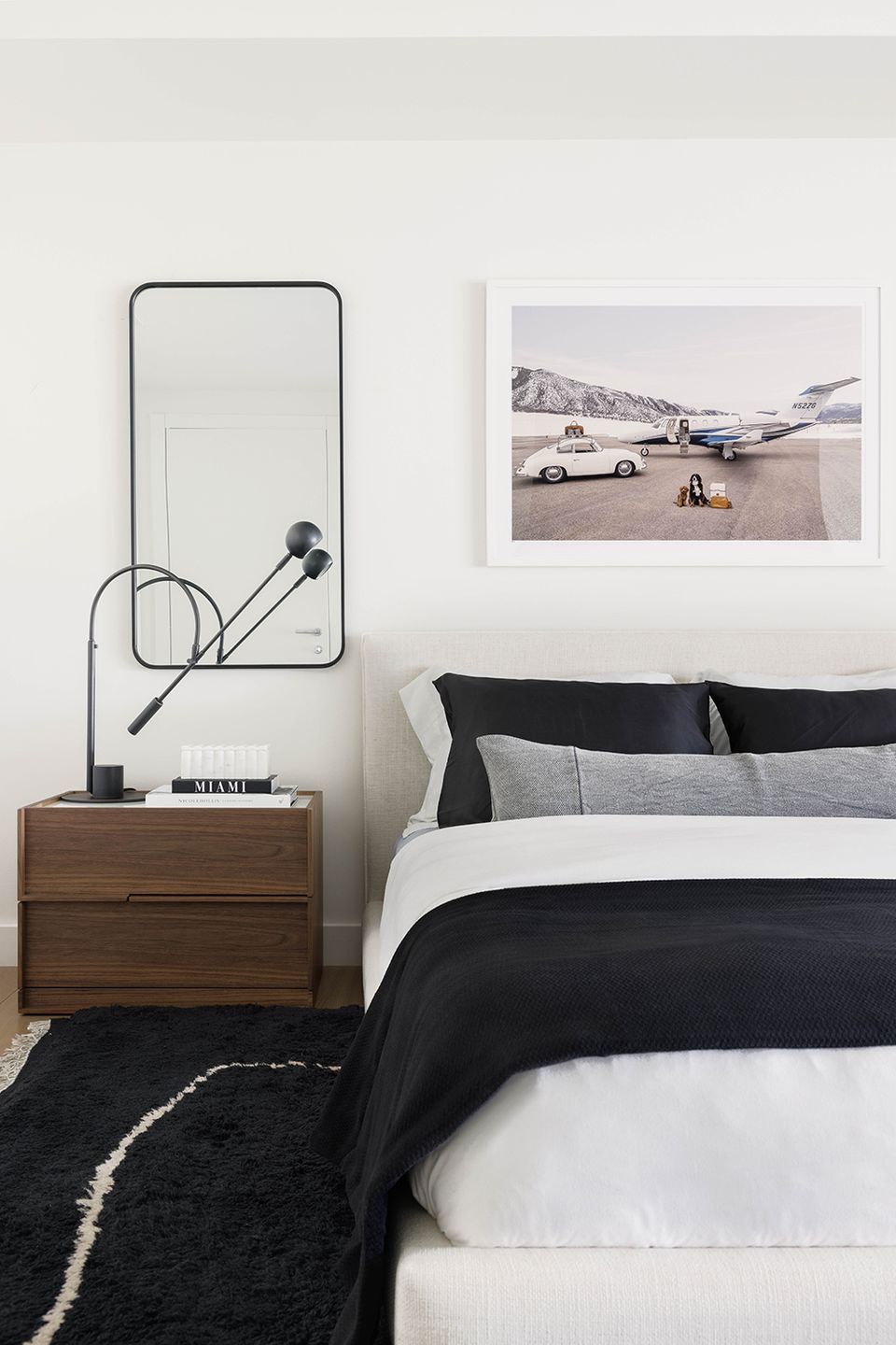 Minimalist black and white bedroom with mid-century wood nightstand, geometric mirror, and vintage roadside photography