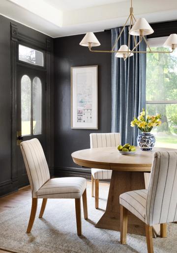 Modern coastal dining with navy walls, natural wood table, and crisp striped upholstery