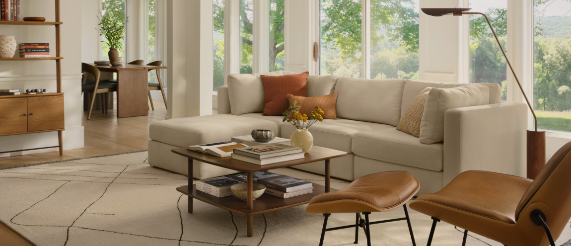 A sunlit living room with a cream sectional, a walnut coffee table, leather lounge chairs and a woven rug
