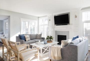 Contemporary coastal living room with fireplace, light wood accents, blue throw pillows, and clean white walls creating an airy aesthetic