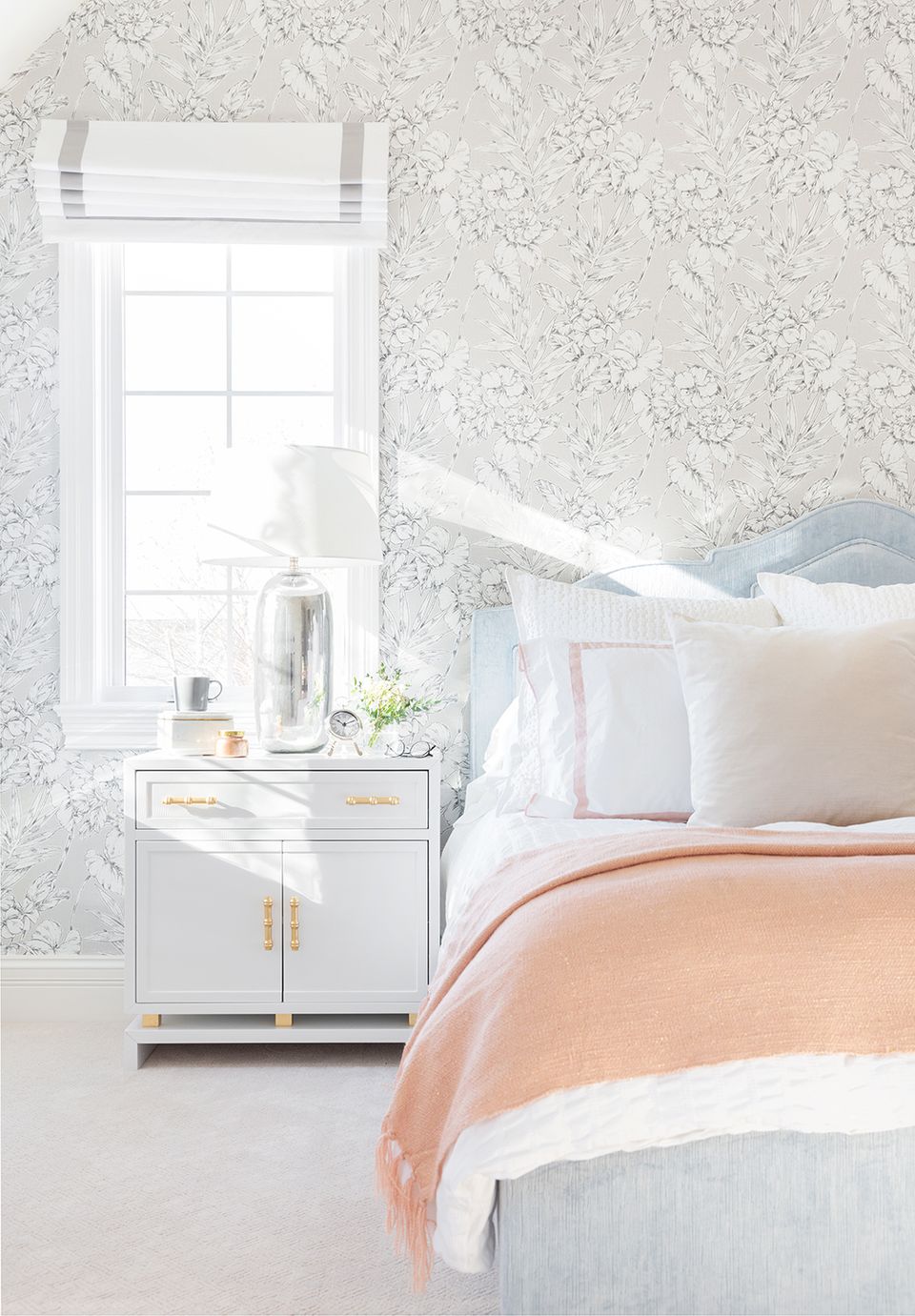 Serene preppy bedroom featuring delicate floral wallpaper, soft peachy bedding, white nightstand with gold hardware, and minimalist coastal-inspired decor